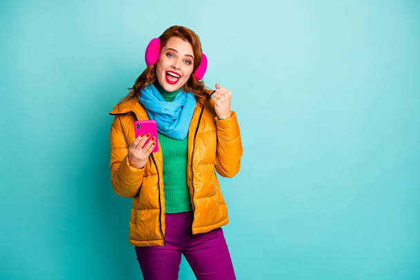 Photo of pretty travel lady hold telephone celebrate achievement first online money income wear trendy casual yellow overcoat scarf purple trousers isolated teal color background - Valokuva, kuva