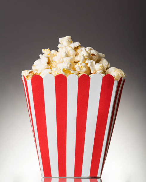 Large striped square box filled with popcorn on gray background. - Foto, imagen