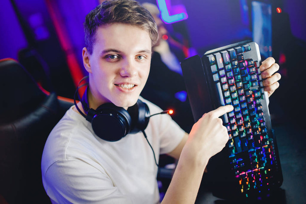 Professional young man player in online video game esport advertises headphones, keyboard and mouse for computer, blurred background - Photo, Image