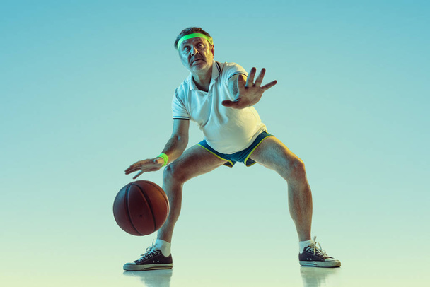 Senior man playing basketball in sportwear on gradient background and neon light - Foto, Imagem