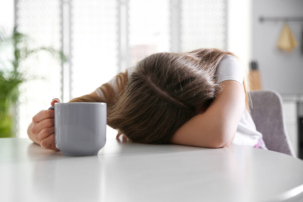 Young woman with cup of drink sleeping at home in morning - Fotoğraf, Görsel