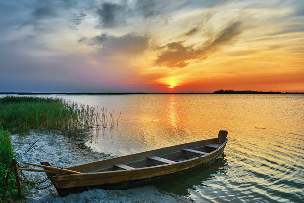 Sunset over the lake - wooden boat on the sandy beach. - Foto, Bild