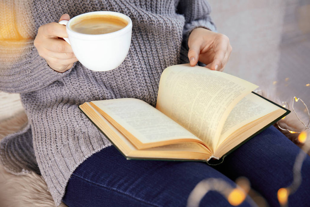 Жінка з чашкою кави читає книгу вдома, крупним планом
 - Фото, зображення