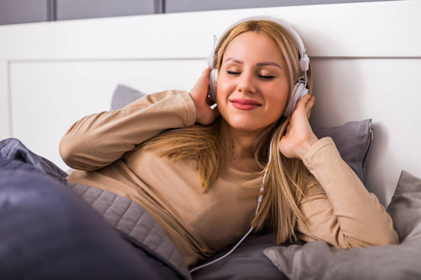 Beautiful woman enjoys listening music and resting in her bed at home. - Foto, Imagem