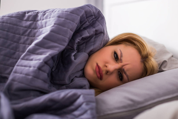 Exhausted woman having fever and lying in her bed all wrapped in duvet. - Photo, Image