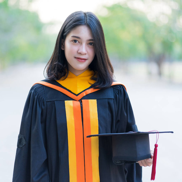 Közelkép portré egy fiatal vidám női diplomás visel akadémiai köntös tartó diplomás sapka ünnepelni egyetemi diplomáját kezdődő napon a főiskolai campus. - Fotó, kép