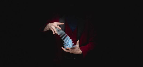 Magician shows trick with playing cards, dark background - Foto, Bild