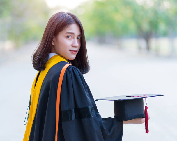Primer plano retrato de una joven y alegre graduada vestida con vestido académico con gorra de graduado celebrar su título universitario en el día de inicio en el campus universitario
. - Foto, Imagen