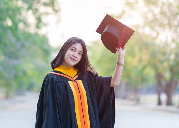 Close up retrato de uma jovem alegre graduada vestindo vestido acadêmico segurando tampa de pós-graduação comemorar seu diploma universitário no dia de início no campus universitário
. - Foto, Imagem