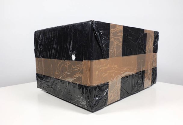 Small black packet or parcel for mail shipping on a white table with elegant grey background - Φωτογραφία, εικόνα