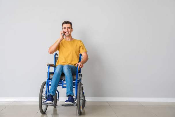 光の壁の近くで電話で話す車椅子の若い男の障害者 - 写真・画像