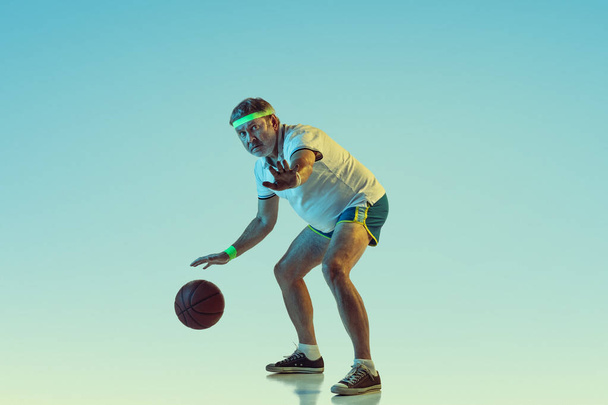 Senior man playing basketball in sportwear on gradient background and neon light - 写真・画像
