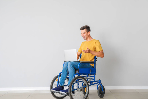 Młody niepełnosprawny mężczyzna na wózku inwalidzkim z laptopem przy ścianie - Zdjęcie, obraz