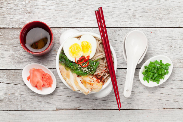 Asiatische Nudel-Ramen-Suppe mit Huhn, Gemüse und Eiern und Kräutertee auf hölzernem Hintergrund. Draufsicht flach gelegt - Foto, Bild