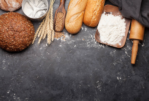 Various bread with wheat, flour and utensils on stone table. Homemade cooking concept. Top view flat lay with copy space - Photo, Image
