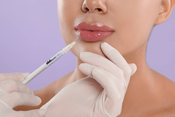 Young woman getting lips injection on lilac background, closeup - Foto, imagen