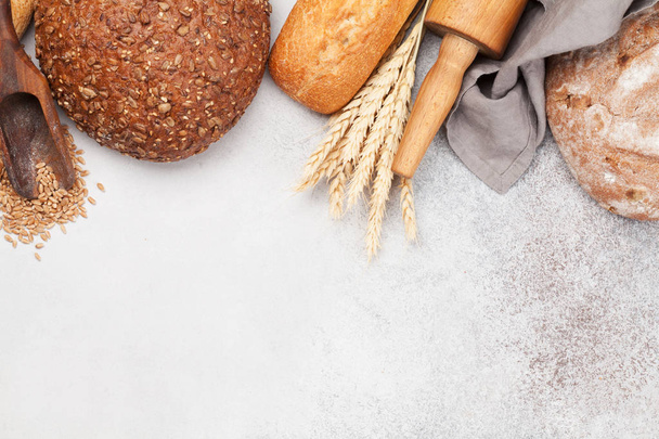 Various bread with wheat and cooking utensils on stone table. Top view flat lay with copy space - Foto, Imagen