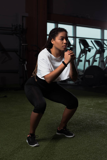 African american attractive woman clenching hands and squating in gym - Foto, immagini