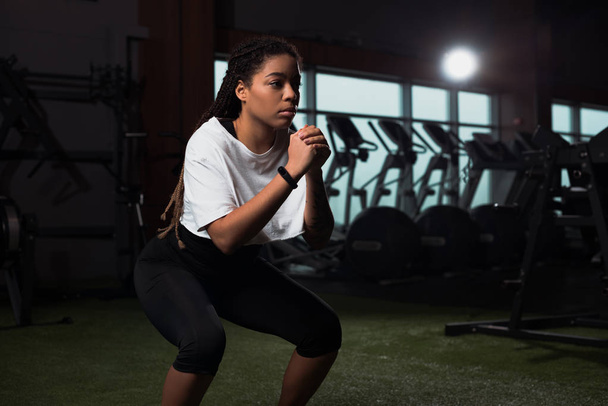 African american woman clenching hands and squating in gym - Photo, Image