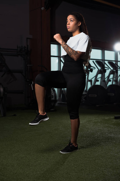 African american woman raising leg and hand while warming up in gym - Foto, imagen