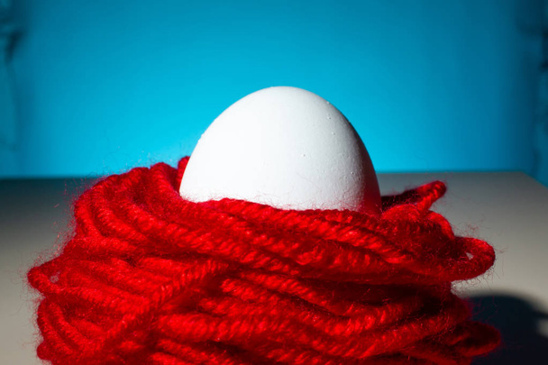 ovo de galinha branco em fios vermelhos fundo azul, close up, espaço de cópia
 - Foto, Imagem