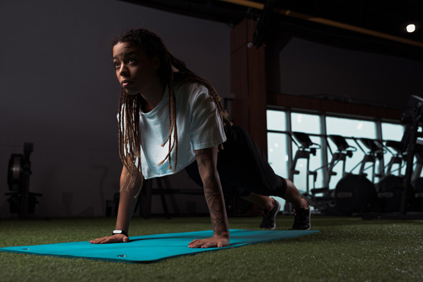 Αφροαμερικανή που στέκεται σε σανίδα στο στρώμα γυμναστικής - Φωτογραφία, εικόνα