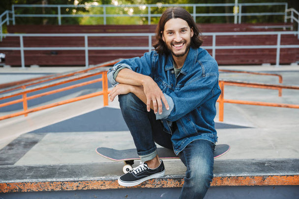 Attractive young hipster man sitting at the skate ramp - Фото, изображение