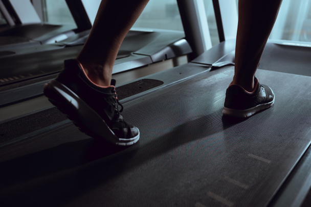 Cropped view of african american woman legs wearing sneakers on treadmill in gym - Foto, imagen