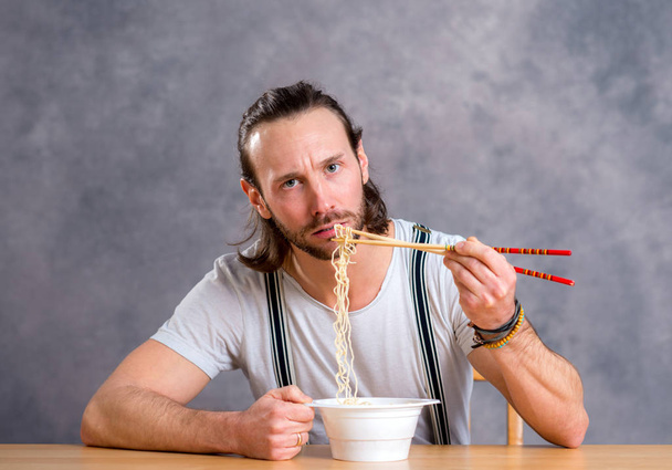 young man eating asian food in front of gray background - Foto, Bild