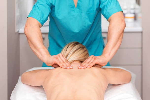 Handen van een massagetherapeut die rugmassage van een vrouw doet. Jonge vrouw met een lichaam beeldhouwprocedure. chiropractie in de rug. Osteopathie, alternatieve geneeskunde, pijn verlichting concept. - Foto, afbeelding