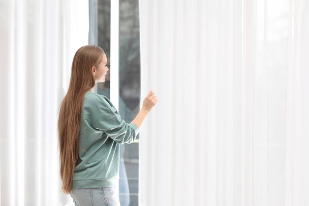 Beautiful young woman looking out of window at home - Photo, image