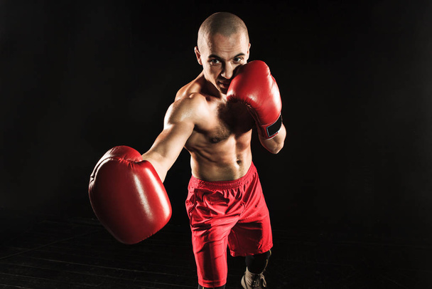 The young male athlete kickboxing on a black background - Фото, изображение