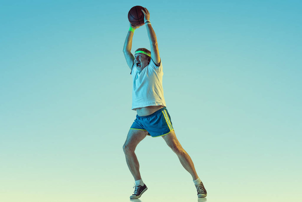 Senior man playing basketball in sportwear on gradient background and neon light - Foto, afbeelding
