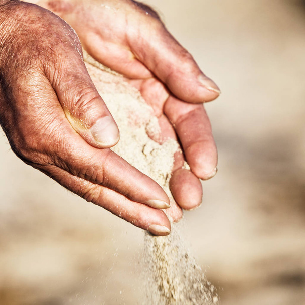 Old man hands holding and spilling sand. Shallow DOF - Фото, изображение