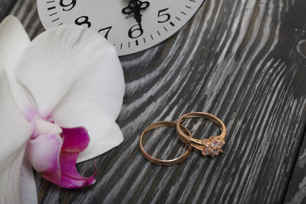 Wedding rings, orchid flower and watch. On brushed pine boards painted in black and white. - Fotografie, Obrázek