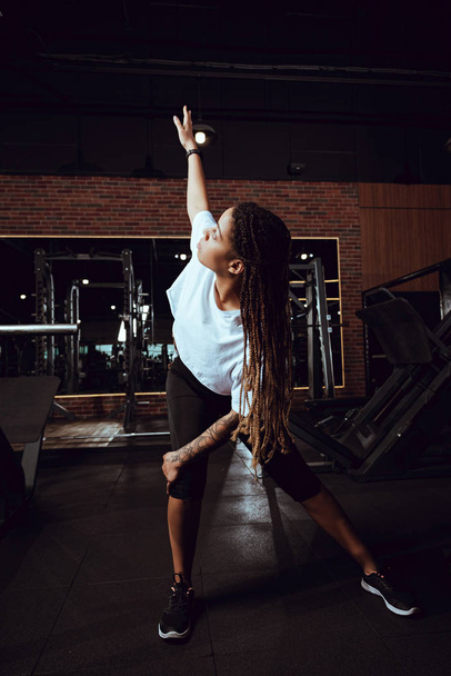 Afrikaans amerikaanse vrouw met dreadlocks stretching in de sportschool  - Foto, afbeelding