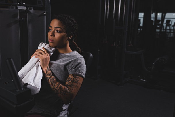 wytatuowana Afroamerykanka trzymająca ręcznik w pobliżu urządzenia fitness - Zdjęcie, obraz
