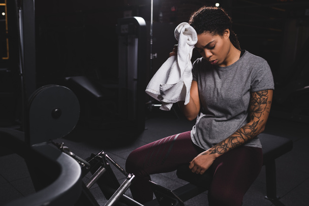 tired african american girl with tattoo wiping sweat with towel  - Photo, Image
