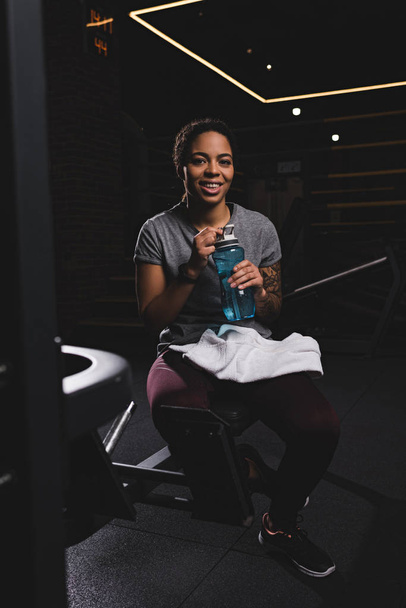 heureux afro-américaine fille avec tatouage tenant bouteille de sport avec de l'eau
  - Photo, image