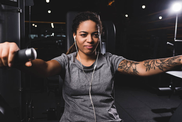 selektivní zaměření šťastné a tetované africké Američanky poslech hudby v tělocvičně  - Fotografie, Obrázek