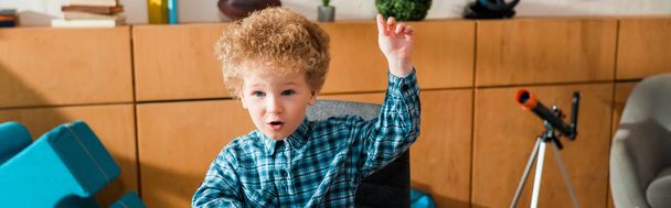 panoramic shot of emotional smart kid with raised hand at home - Fotografie, Obrázek