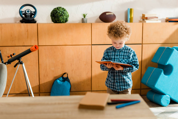 επιλεκτική εστίαση του βιβλίου έξυπνο παιδί ανάγνωση, ενώ στέκεται στο σπίτι - Φωτογραφία, εικόνα