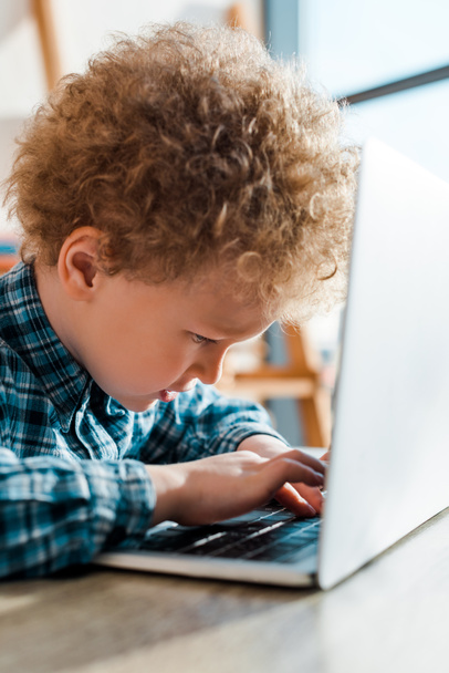 selective focus of curly kid typing on laptop keyboard  - Foto, Imagem
