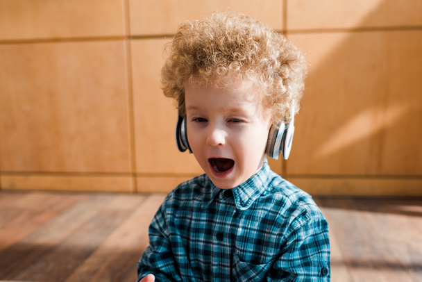 exhausted kid listening music in wireless headphones and yawning at home - Foto, afbeelding