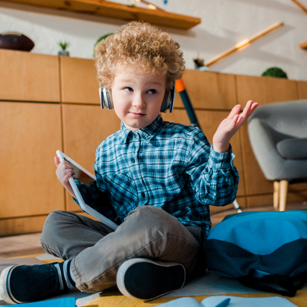 szelektív fókusz zavaros gyerek fülhallgató kezében digitális táblagép és mutatja vonagló gesztus  - Fotó, kép
