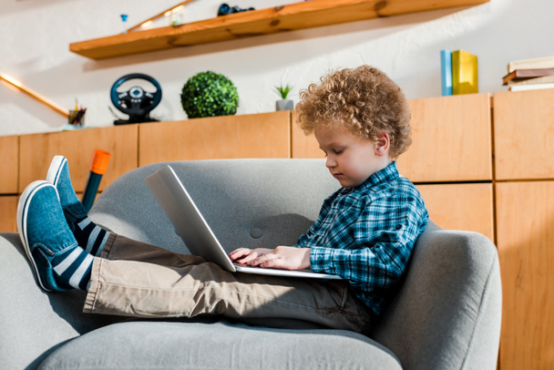 cute kid sitting in armchair and using laptop  - Photo, Image