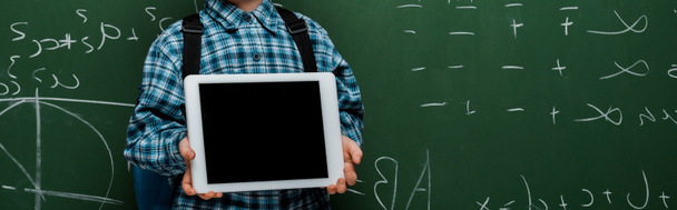 panoramic shot of smart kid holding digital tablet with blank screen near chalkboard with mathematical formulas  - Фото, зображення
