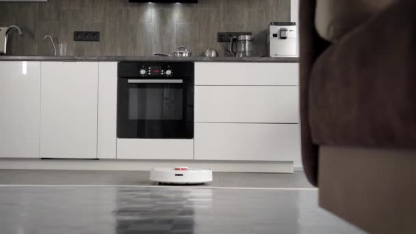 In a stylish modern kitchen is cleaning. The automatic robot vacuum cleaner moves along its trajectory. Elements of a smart home make life easier for people - Séquence, vidéo