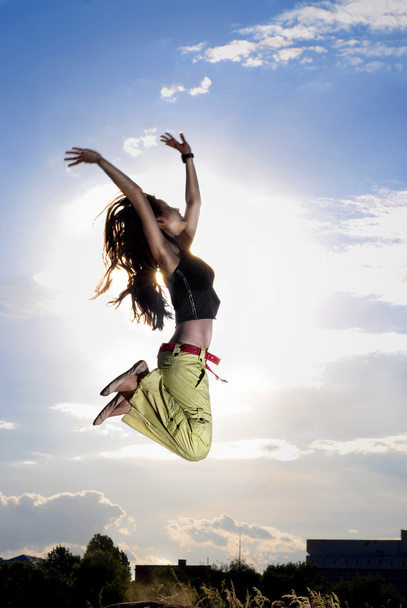 A young girl jumping in front of blue sky and sun - Фото, зображення