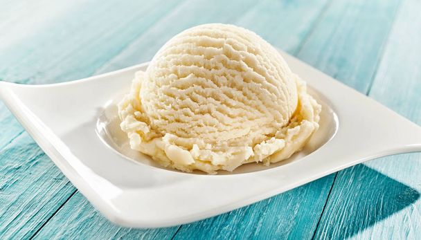 Serving of delicious frozen creamy vanilla ice cream on a modern rectangular plate outdoors on a blue rustic picnic table for summer dessert - Φωτογραφία, εικόνα